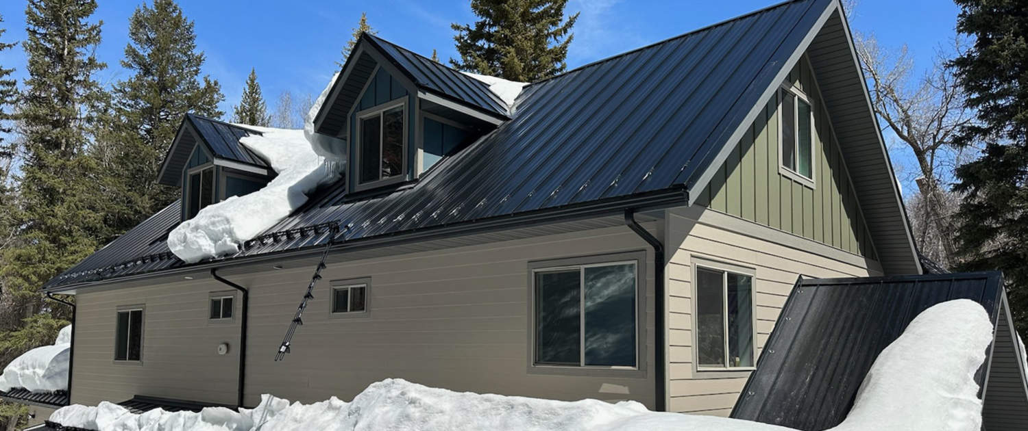 Side view of snow covering a dark metal roof and surrounding area