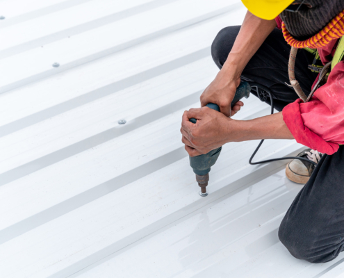 Side view of a roofer screwing in a metal roof